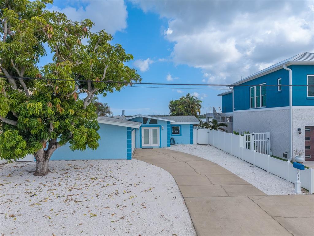 A bright blue single-story house features a concrete driveway and a large tree in front — 814 BAY POINT DRIVE, MADEIRA BEACH, FL