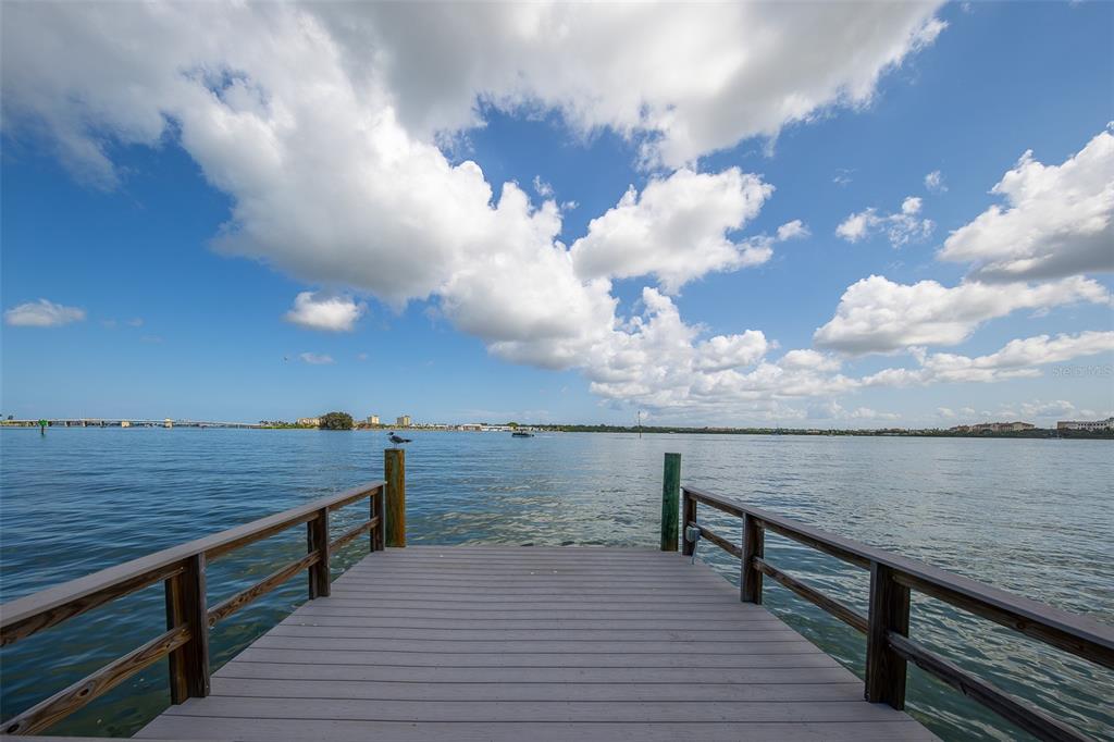 A wooden dock extends over a calm body of water under a bright, cloudy sky — 814 BAY POINT DRIVE, MADEIRA BEACH, FL
