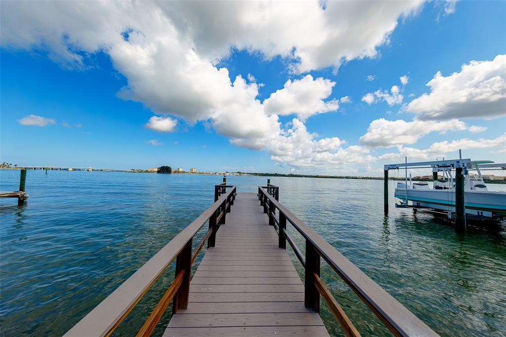 A wooden dock extends over the water toward a distant bridge under a cloudy sky — 814 BAY POINT DRIVE, MADEIRA BEACH, FL