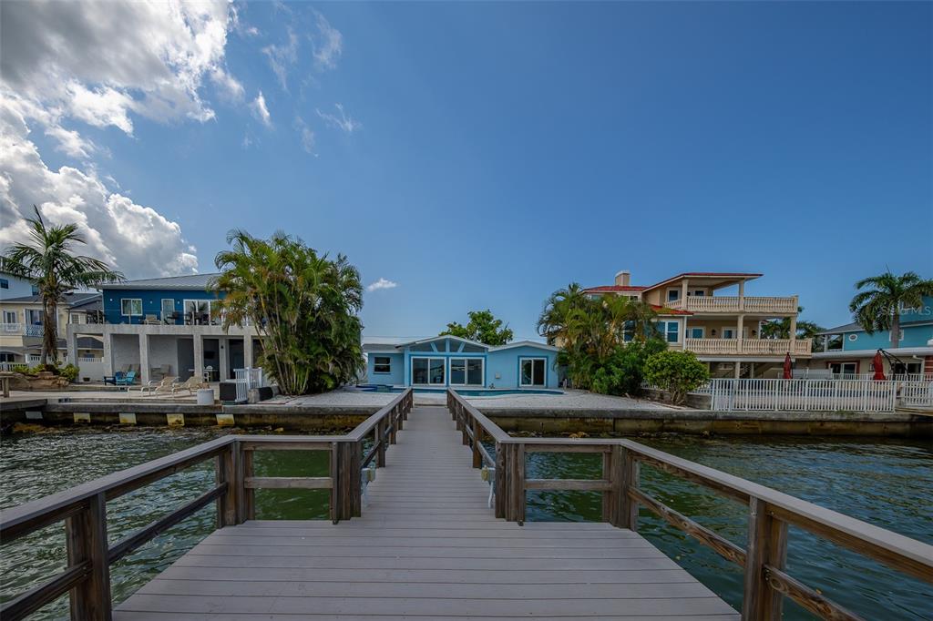 A wooden dock leads toward a light blue waterfront house with a backyard swimming pool — 814 BAY POINT DRIVE, MADEIRA BEACH, FL