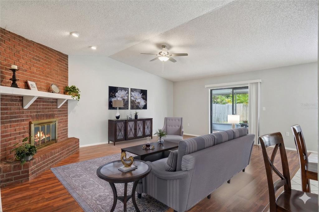 A living room features a brick fireplace, wood flooring, a ceiling fan, and sliding doors — 105 LOTUS CIRCLE, SAFETY HARBOR, FL