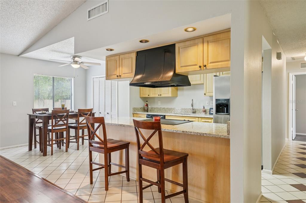 A kitchen with light wood cabinets, granite countertops, and a black range hood overlooks a dining area — 105 LOTUS CIRCLE, SAFETY HARBOR, FL