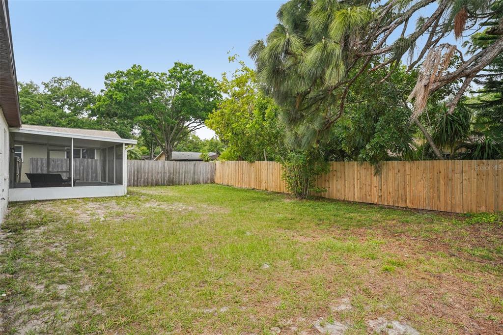 A grassy backyard features a screened-in patio and a tall wooden privacy fence — 105 LOTUS CIRCLE, SAFETY HARBOR, FL