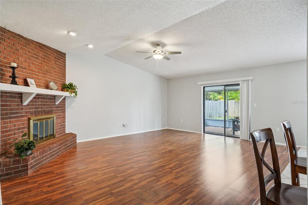 A living room with a brick fireplace, wood-look flooring, a ceiling fan, and sliding glass doors — 105 LOTUS CIRCLE, SAFETY HARBOR, FL