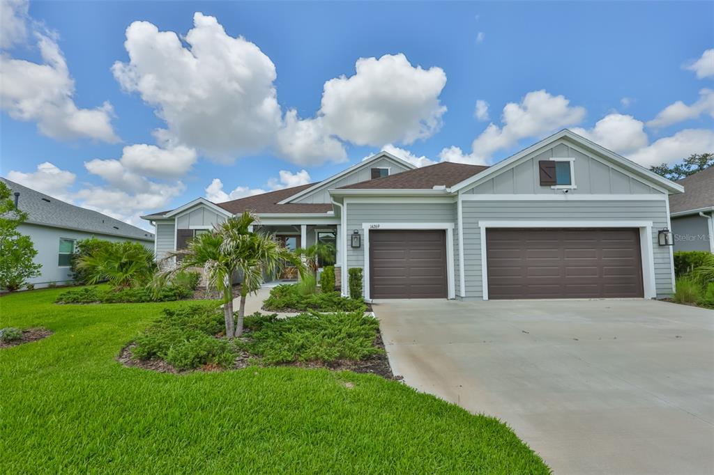 A single-story house with light green siding, a three-car garage, and a landscaped front yard — 14269 SKIPPING STONE LOOP, PARRISH, FL