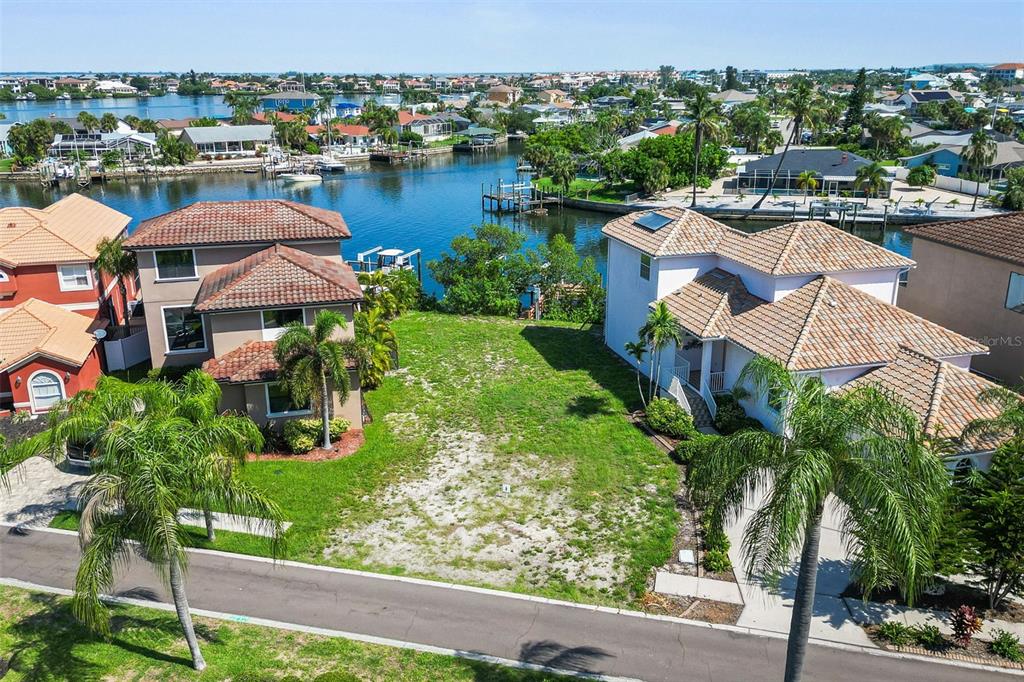 An aerial view shows a vacant waterfront lot situated between two multi-story residential homes — 873 SYMPHONY ISLES BOULEVARD, APOLLO BEACH, FL