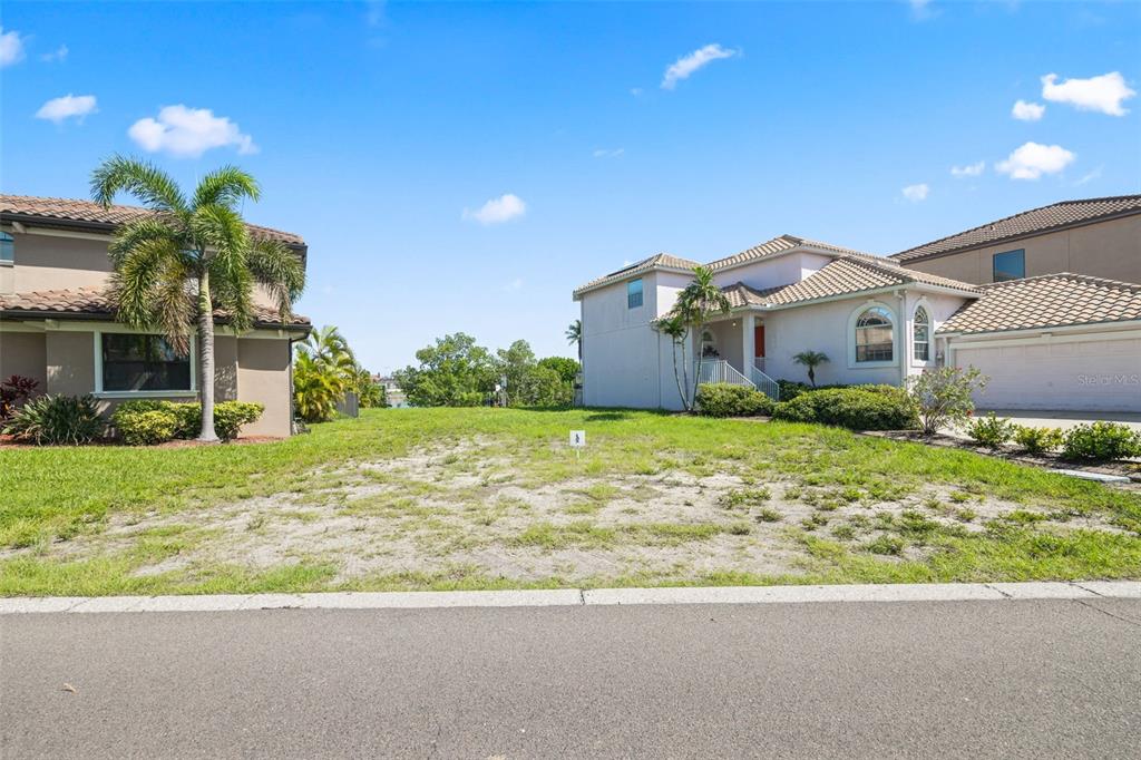 A vacant residential lot sits between two multi-story houses under a clear blue sky — 873 SYMPHONY ISLES BOULEVARD, APOLLO BEACH, FL