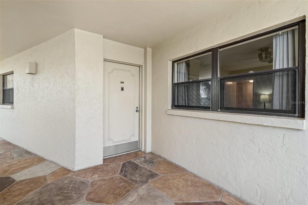 A white front door and a large window are set into a textured beige exterior wall — 8770 MIDNIGHT PASS ROAD UNIT 402B, SARASOTA, FL