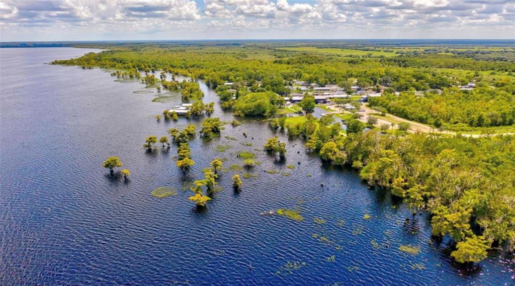 An aerial view shows a lake with cypress trees near a wooded shoreline and buildings — 21722 73RD LANE, VERO BEACH, FL