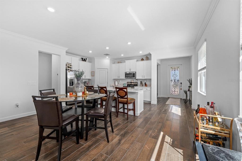 A dining area with a round table and kitchen with white cabinets and wood flooring — 10314 BANYAN BREEZE BOULEVARD, LAND O LAKES, FL