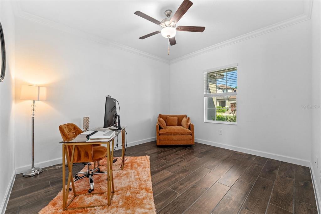 A home office features dark wood-look tile flooring, a glass desk, and an orange armchair — 10314 BANYAN BREEZE BOULEVARD, LAND O LAKES, FL