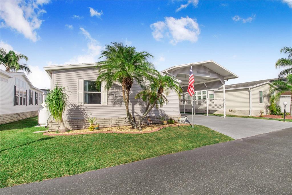 A light-colored manufactured home features a palm tree, a carport, and an American flag — 332 FAIRWAY BOULEVARD, FROSTPROOF, FL