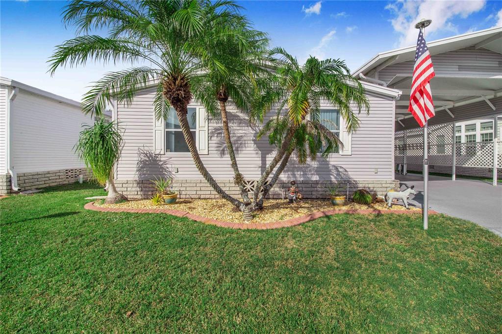 A light-colored mobile home features a palm tree in the front yard and an American flag — 332 FAIRWAY BOULEVARD, FROSTPROOF, FL