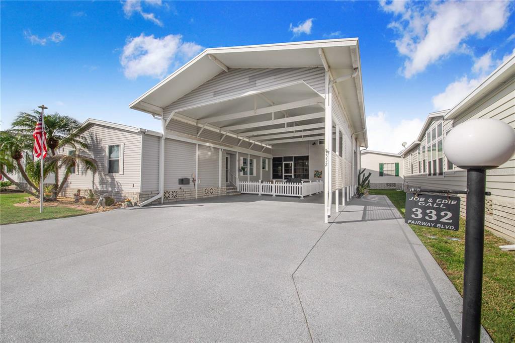 A manufactured home features a large concrete driveway, a covered carport, and a white fence — 332 FAIRWAY BOULEVARD, FROSTPROOF, FL