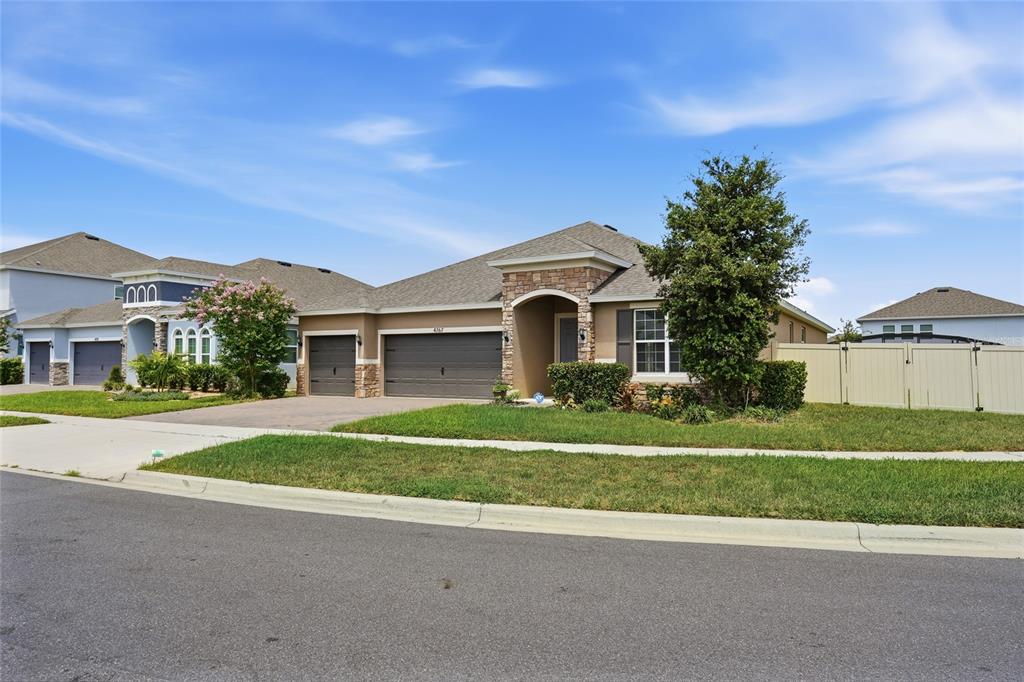 A single-story suburban house with a tan stucco exterior, stone accents, and a three-car garage — 4767 CRAGMERE LOOP, CLERMONT, FL