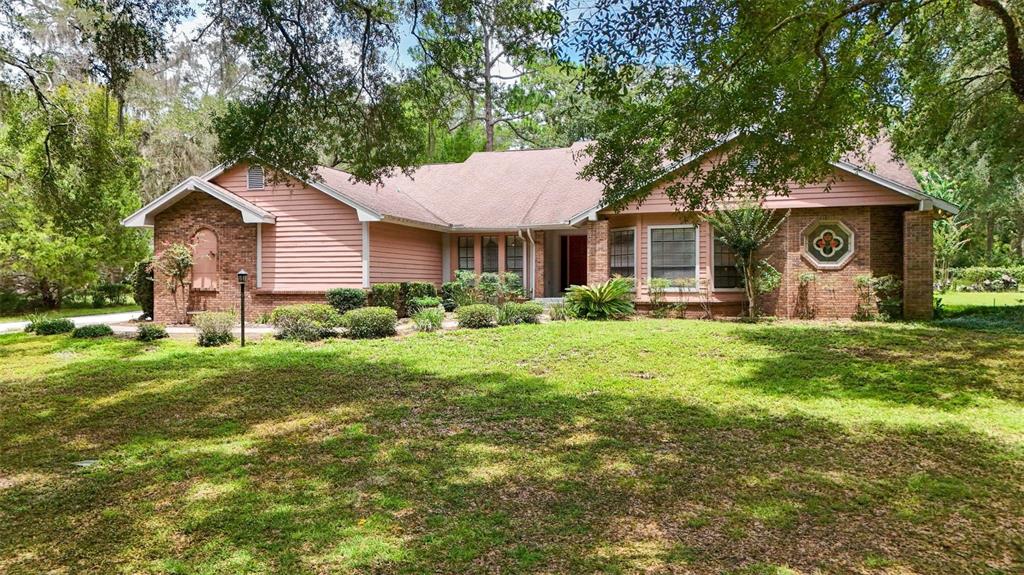 A single-story house with brick and pink siding features a large front lawn and trees — 2705 W LIVE OAK STREET, LECANTO, FL