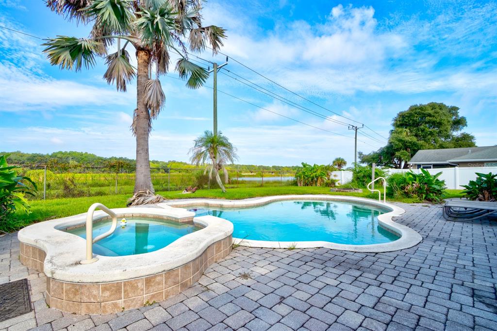 A backyard swimming pool and attached hot tub sit on a paved patio with palm trees — 1026 LAKE AVENUE, EDGEWATER, FL