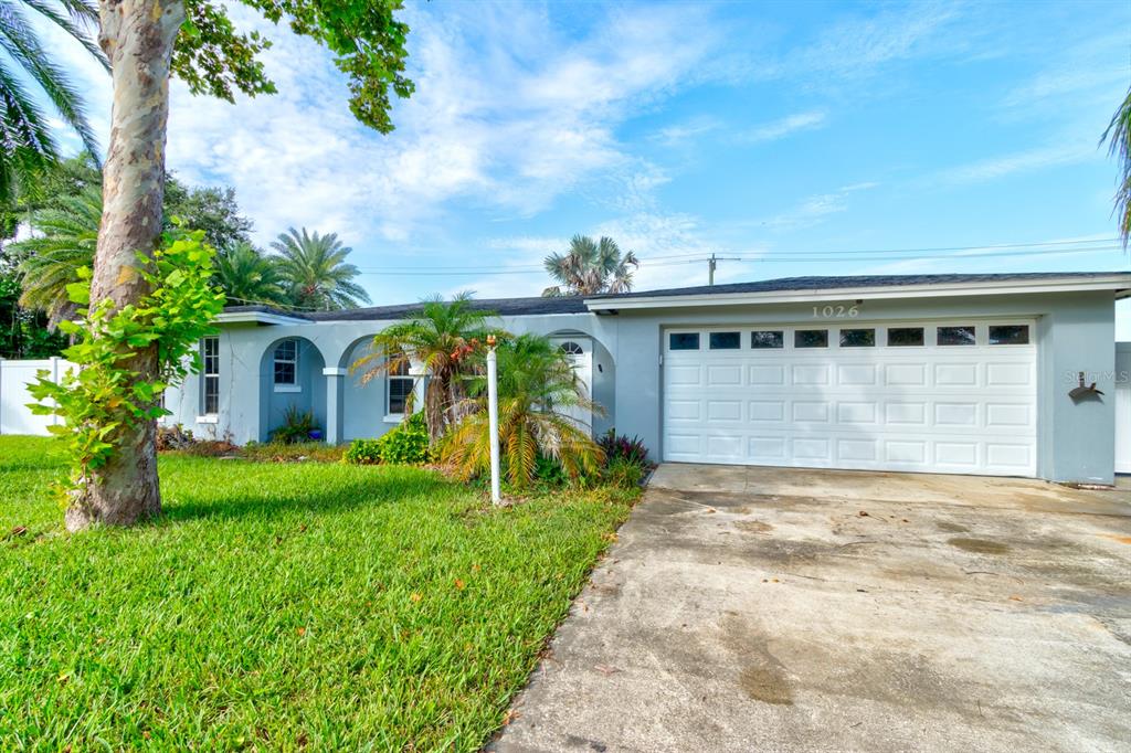 A single-story house with a white garage door, arched entryway, and a large front lawn — 1026 LAKE AVENUE, EDGEWATER, FL