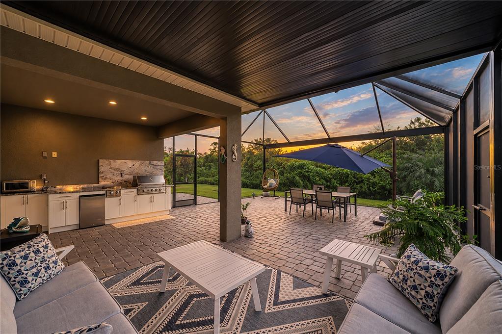A covered outdoor patio features a kitchen, dining area, and seating space with a screened enclosure — 5440 HOPE SOUND CIRCLE, SARASOTA, FL