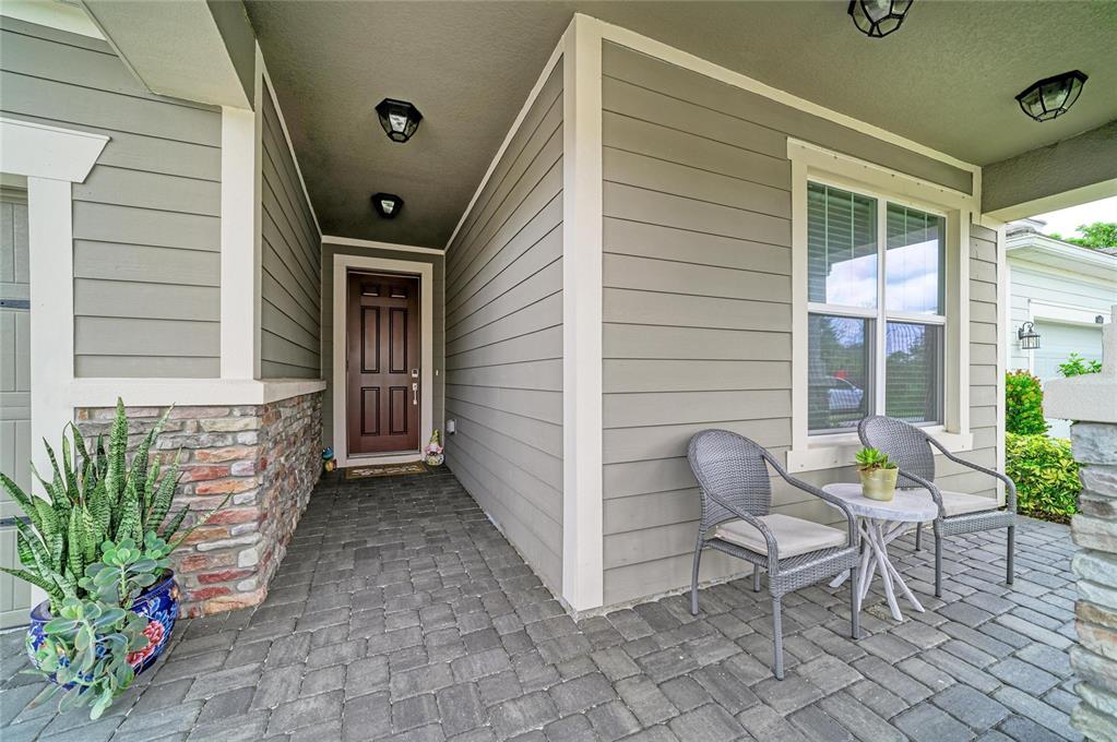 A covered front porch features gray siding, stone accents, a brown door, and patio furniture — 5440 HOPE SOUND CIRCLE, SARASOTA, FL
