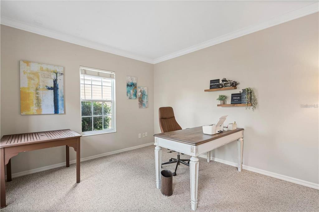 A home office features a desk, chair, wall shelving, and a window with carpeted flooring — 932 PAWSTAND ROAD, CELEBRATION, FL