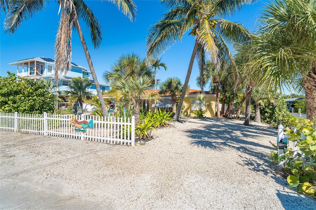 A yellow house with a gravel driveway and palm trees behind a white picket fence — 90 N GULF BOULEVARD, PLACIDA, FL