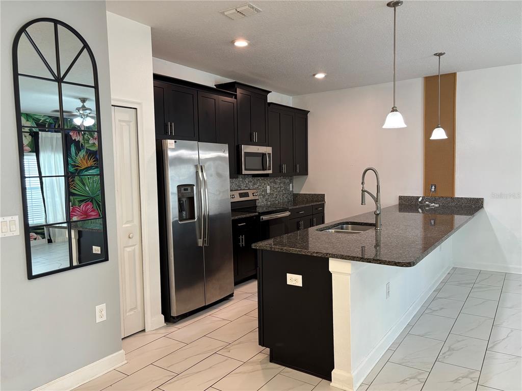 A kitchen features dark cabinets, stainless steel appliances, granite countertops, and a large island — 1591 MOON VALLEY DRIVE, DAVENPORT, FL