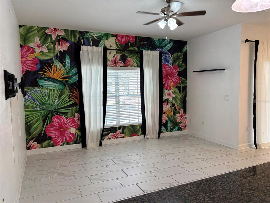 A living room features a tropical floral accent wall, white tile flooring, and a ceiling fan — 1591 MOON VALLEY DRIVE, DAVENPORT, FL