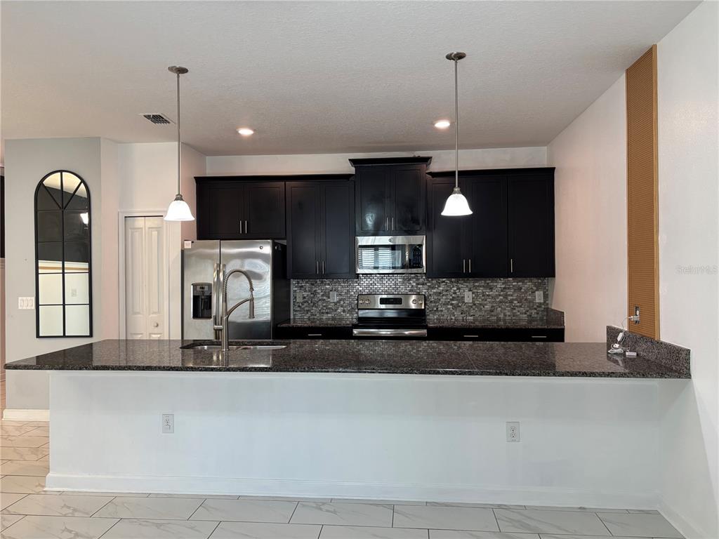 A kitchen features dark cabinets, granite countertops, stainless steel appliances, and a breakfast bar — 1591 MOON VALLEY DRIVE, DAVENPORT, FL