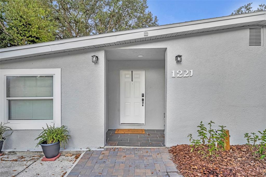 The exterior of a house features a white front door, gray stucco walls, and pavers — 1221 ELINORE DRIVE, ORLANDO, FL