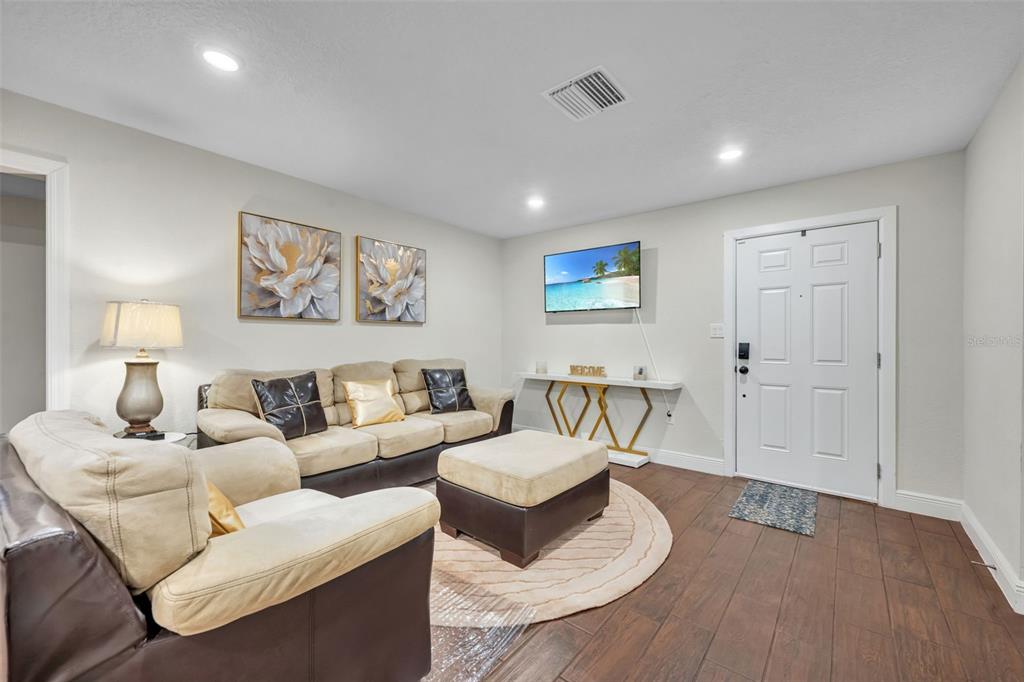 A living room features a beige sofa, a matching ottoman, and a wall-mounted television — 1221 ELINORE DRIVE, ORLANDO, FL