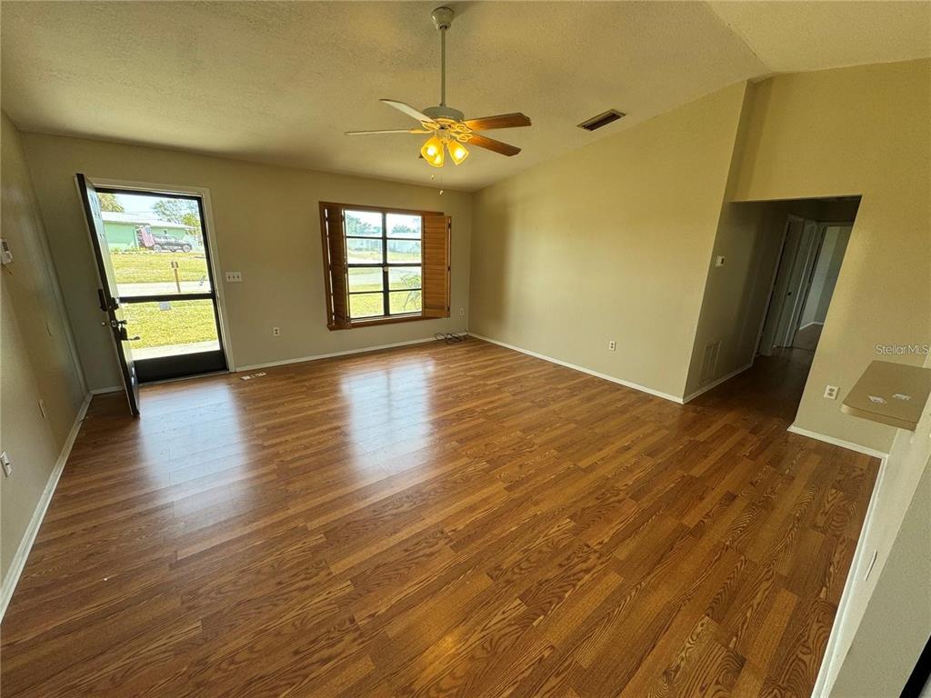 An empty living room features wood-look flooring, a ceiling fan, and a glass-paneled entry door — 1786 DAGON ROAD, VENICE, FL