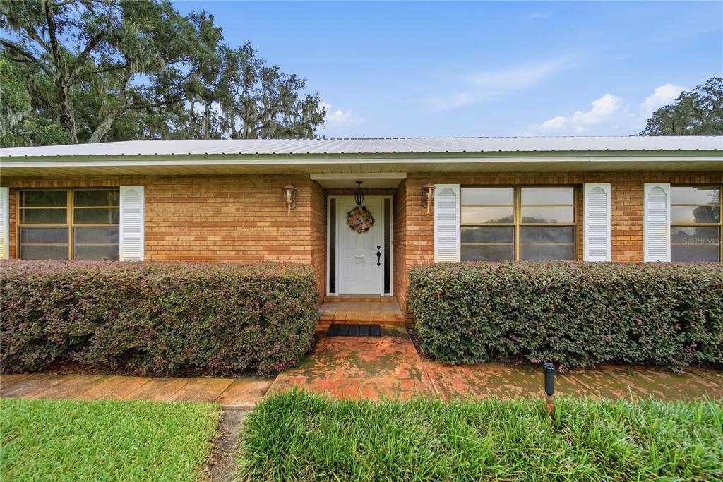 A single-story brick house features a white front door, shuttered windows, and large trimmed hedges — 3704 THONOTOSASSA ROAD, PLANT CITY, FL