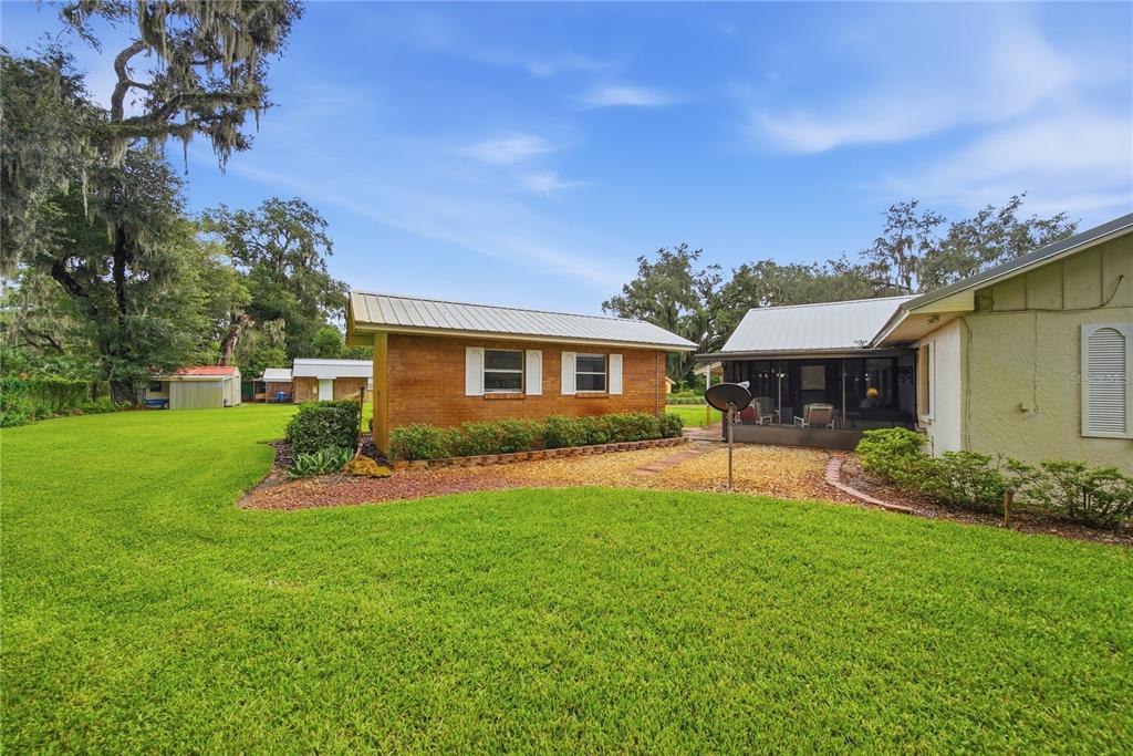 A brick outbuilding sits on a grassy lawn next to a house with a screened porch — 3704 THONOTOSASSA ROAD, PLANT CITY, FL