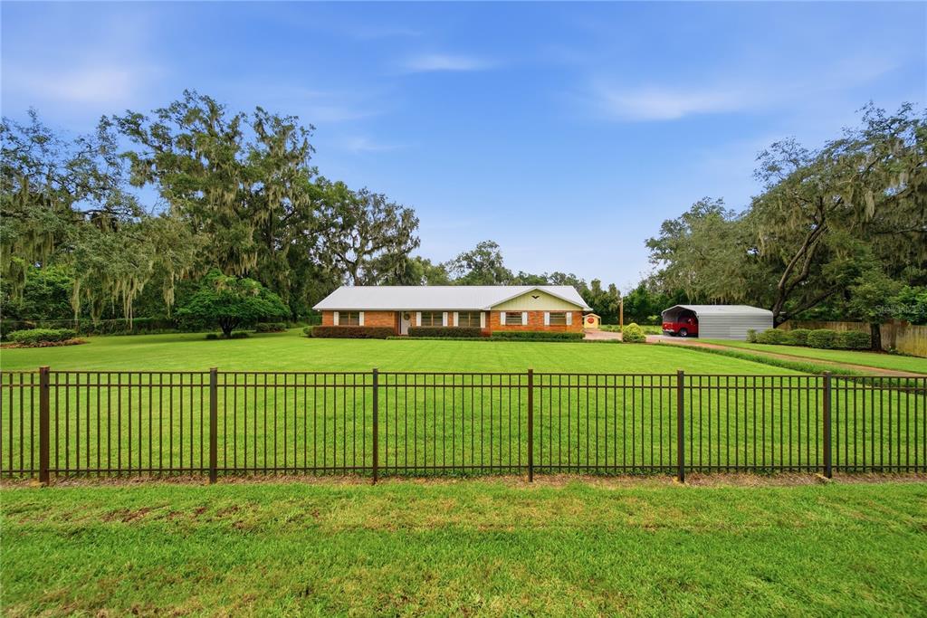 A single-story brick house with a metal roof sits behind a black metal fence — 3704 THONOTOSASSA ROAD, PLANT CITY, FL