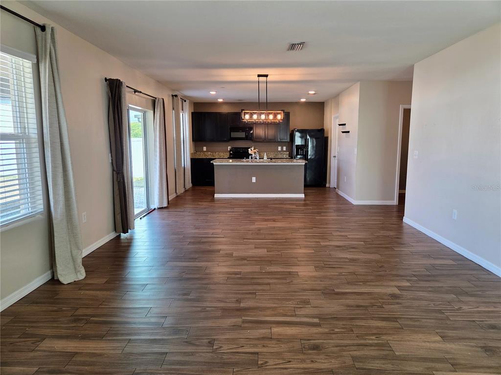 An empty living room features wood-look flooring, beige walls, and two windows with curtains — 109 TIERRA VERDE WAY, BRADENTON, FL