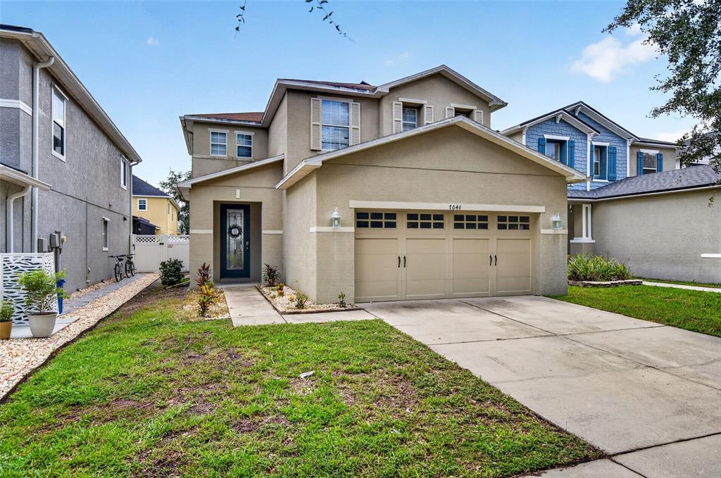A two-story suburban house with a tan stucco exterior and a two-car garage — 7046 PENTA PLACE, WESLEY CHAPEL, FL