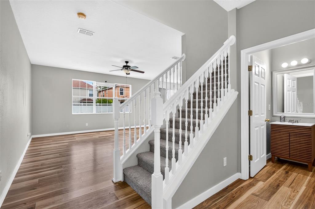 A staircase with gray carpet and white railings stands next to a bathroom and living area — 7046 PENTA PLACE, WESLEY CHAPEL, FL
