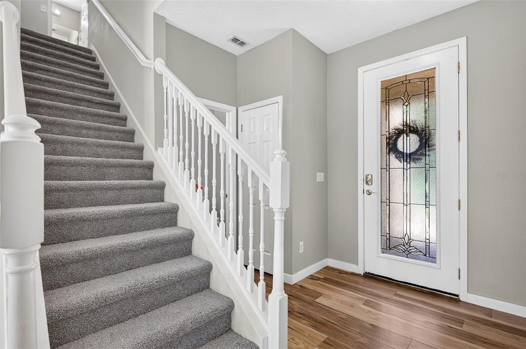 A carpeted staircase with a white railing stands next to a front door with glass — 7046 PENTA PLACE, WESLEY CHAPEL, FL