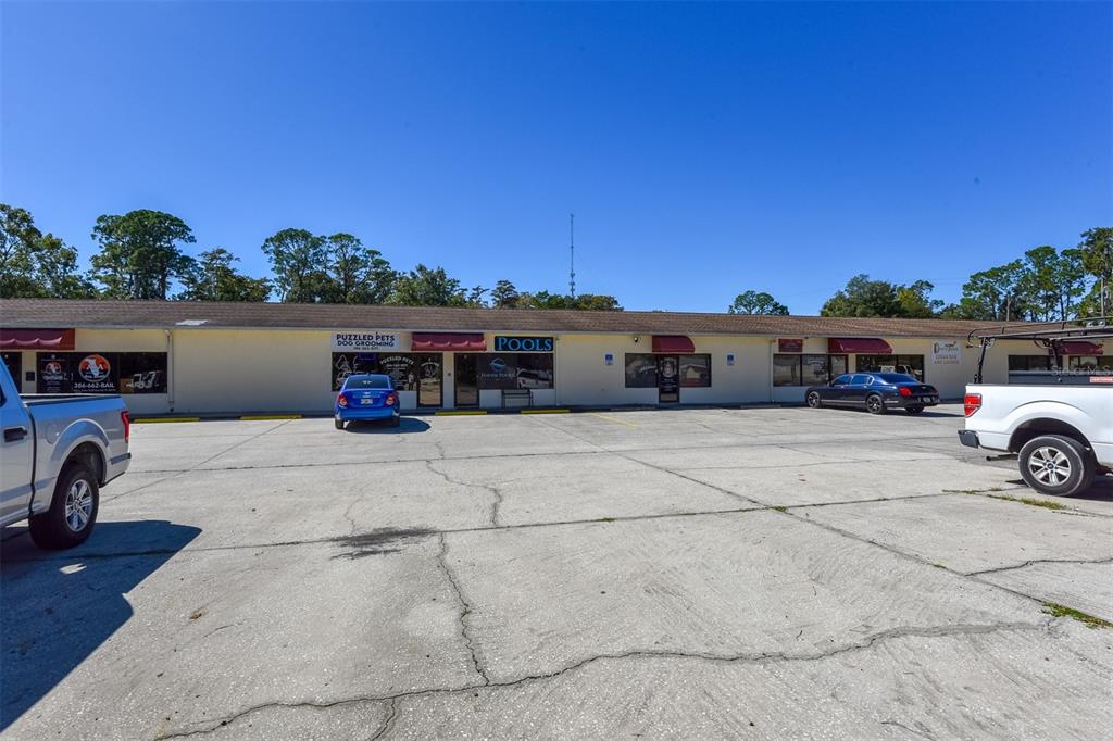 A single-story commercial strip mall with a parking lot in front under a clear sky — 703 S STATE STREET, BUNNELL, FL
