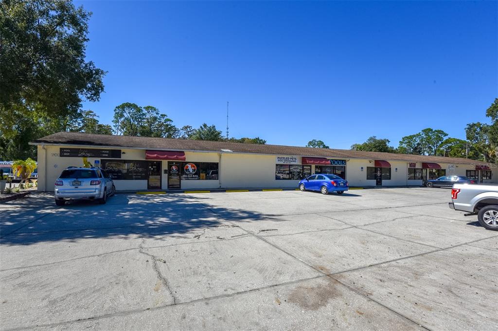 A single-story commercial strip mall with a large concrete parking lot under a clear sky — 703 S STATE STREET, BUNNELL, FL