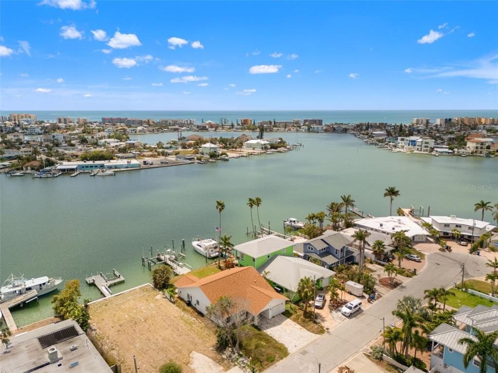 An aerial view shows waterfront homes, docks, boats, and a bay under a blue sky — 811 BAY POINT DRIVE, MADEIRA BEACH, FL