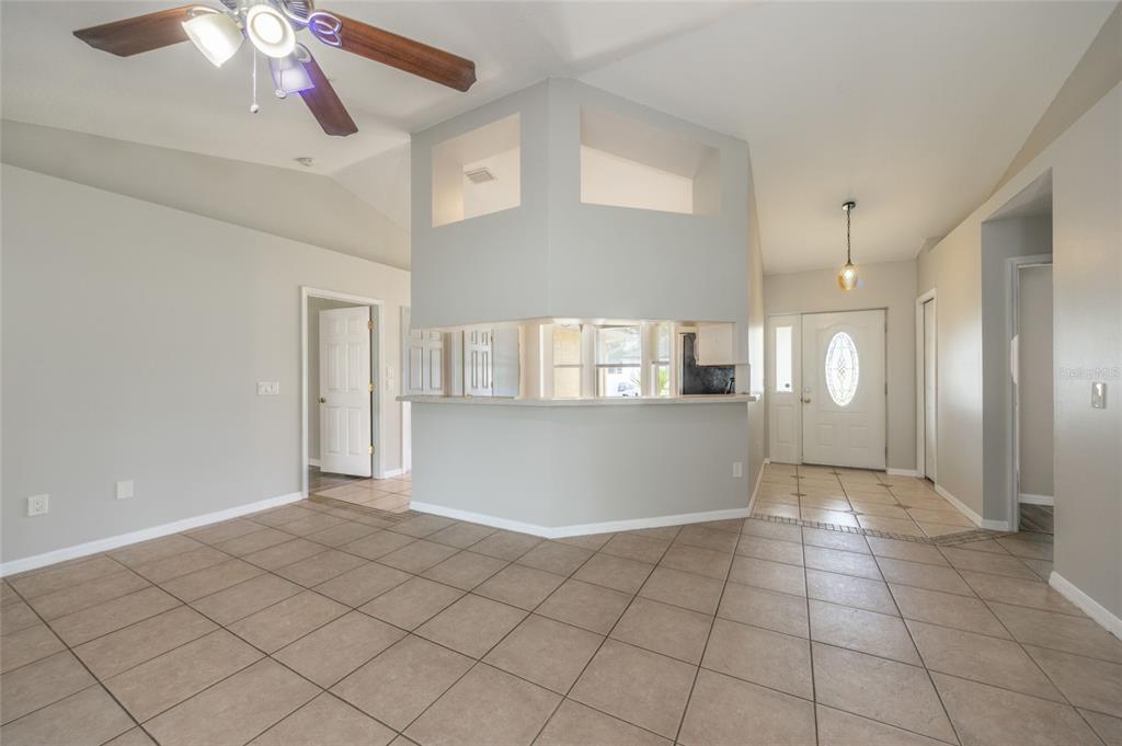 A living room with beige tile flooring, a vaulted ceiling, a ceiling fan, and sliding doors — 37 ROCKEFELLER DRIVE, PALM COAST, FL