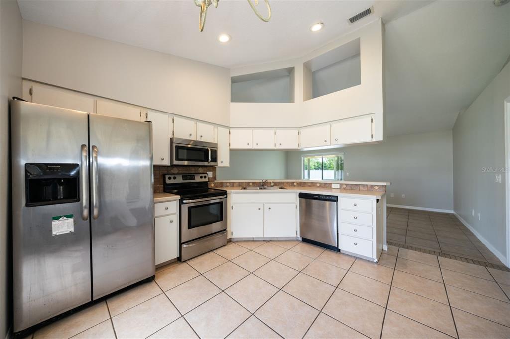 A kitchen with white cabinets, stainless steel appliances, tile flooring, and a breakfast nook area — 37 ROCKEFELLER DRIVE, PALM COAST, FL