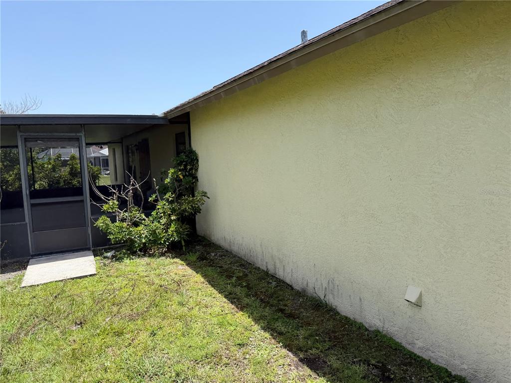 A view of a yellow stucco exterior wall next to a screened-in patio area — 8451 SW 14TH LANE, OKEECHOBEE, FL