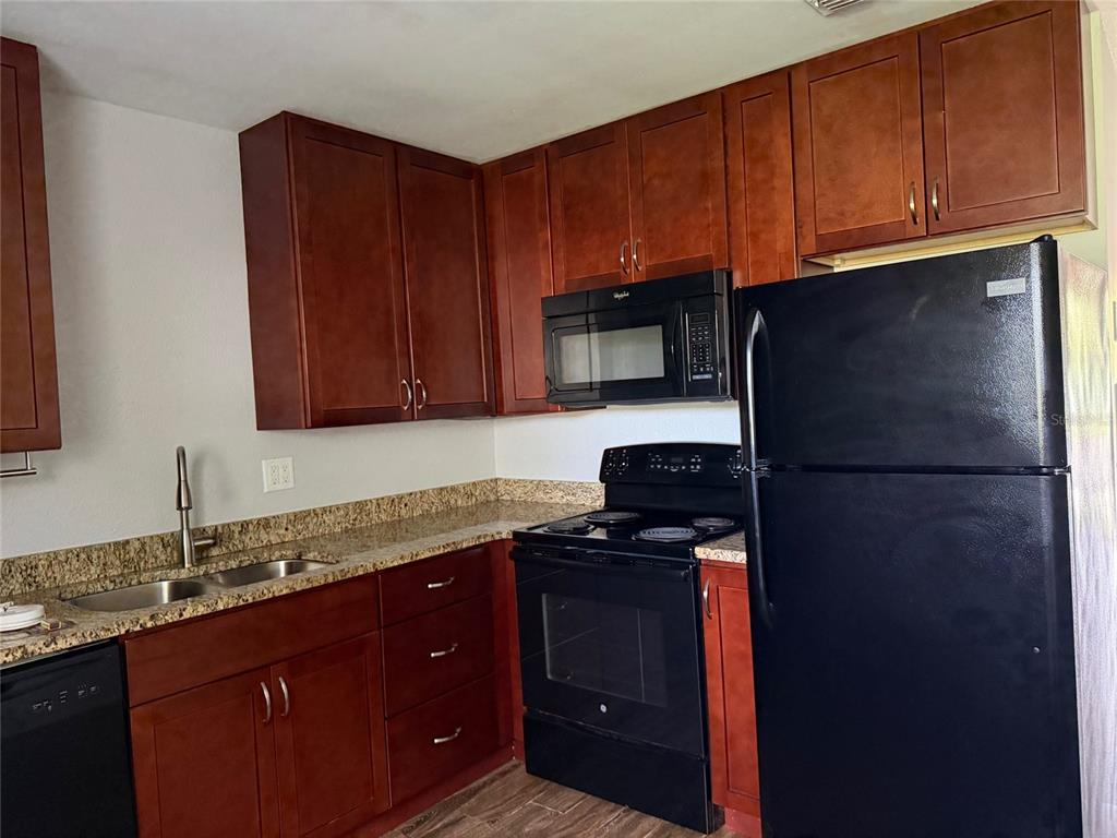 A kitchen features dark wood cabinets, granite countertops, and black appliances — 502 VARSITY STREET, WINTER GARDEN, FL