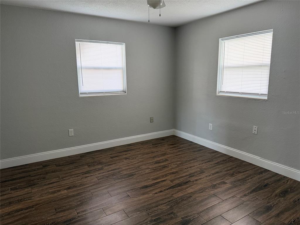 An empty room features gray walls, dark wood-look flooring, two windows with blinds, and baseboards — 502 VARSITY STREET, WINTER GARDEN, FL