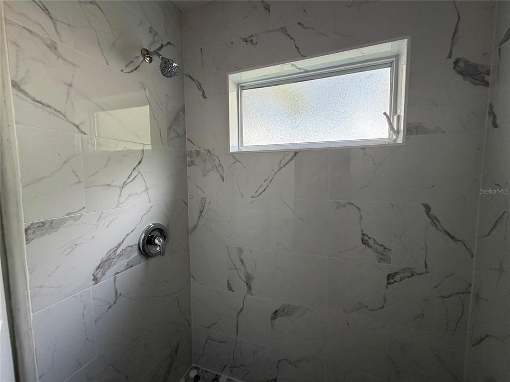 A shower stall features white marble-look wall tiles, a chrome showerhead, and a small window — 502 VARSITY STREET, WINTER GARDEN, FL
