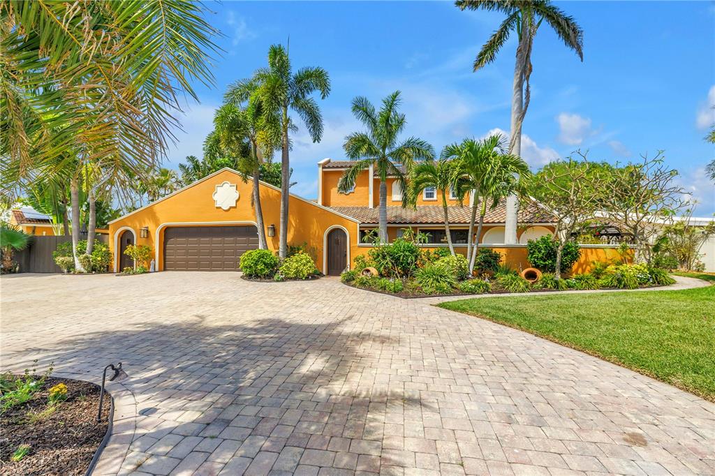 A yellow house with a brown garage door and a paved driveway surrounded by palm trees — 3945 POINSETTIA DRIVE, ST PETE BEACH, FL