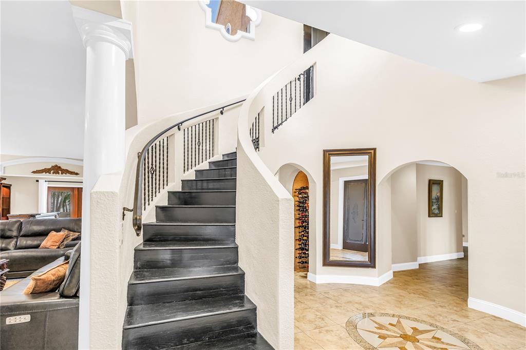 A curved staircase with black treads and iron railings stands in a tiled foyer — 3945 POINSETTIA DRIVE, ST PETE BEACH, FL